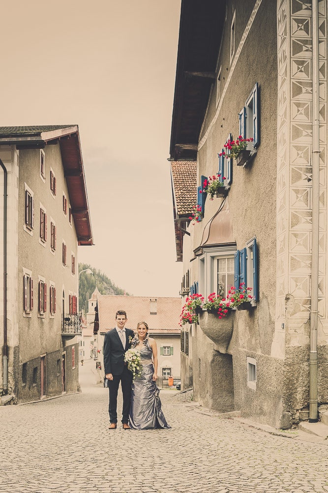 Hochzeitspaar steht in einer engen Gasse im Dorf Bergün.