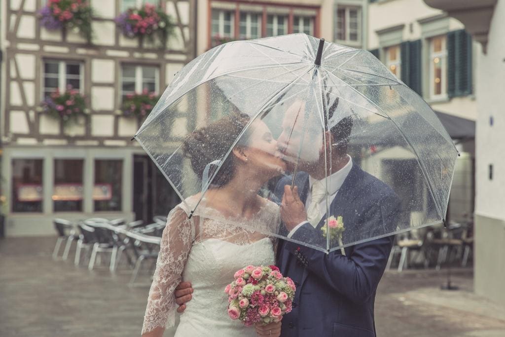 Brautpaar küsst sich hinter einem durchsichtigen Regenschirm in der Altstadt von St.Gallen.